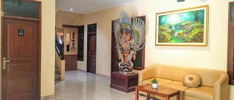 A hotel lobby with a reception desk, a sofa, a decorative statue, and a painting on the wall.