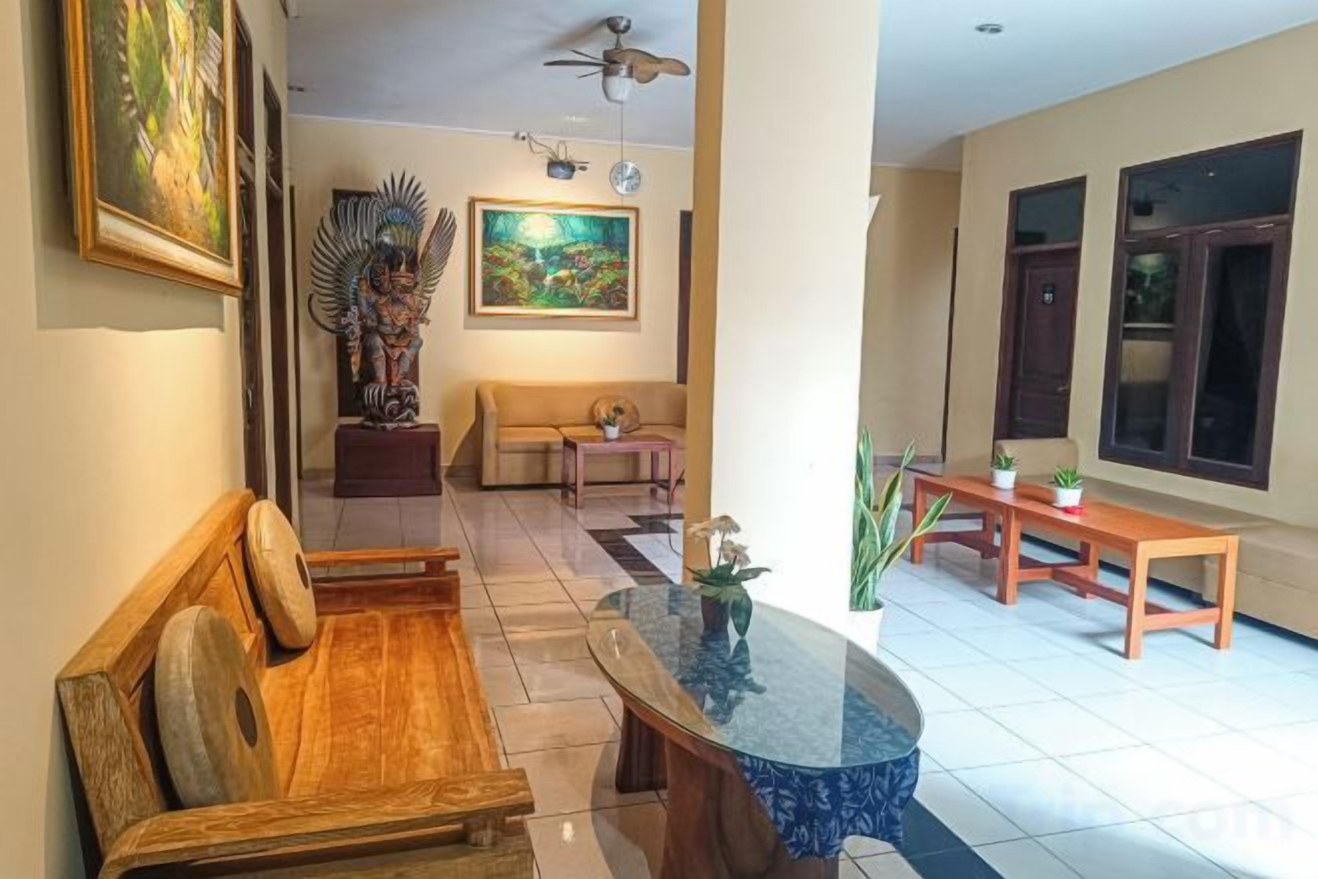 A living room with a sofa, a coffee table, and a dining table. There are paintings on the walls and a ceiling fan.