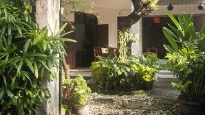 A building entrance with a sign, lush greenery, and a stone pathway. - Miraa Guest House & Resto (Denpasar)