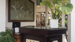 A reception desk with a large painting, a potted plant, and a modern pendant light. - Miraa Guest House & Resto (Denpasar)