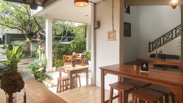 A wooden dining area with tables and chairs, a staircase, and a view of greenery outside. - Miraa Guest House & Resto (Denpasar)