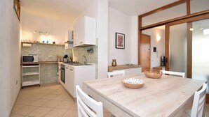 A compact kitchen with a dining area, white cabinetry, a microwave, and a tiled backsplash. - Three-room apartment downtown with two bathrooms and A/C (Santa Teresa Gallura)