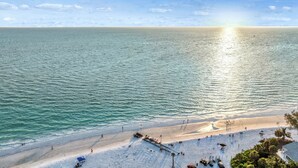 Une plage avec une jetée qui s’avance dans l’eau, des gens qui se promènent le long du rivage et un ciel dégagé.