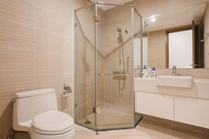 Ein modernes Badezimmer mit einer gläsernen Duschkabine, einer Toilette und einem Waschbecken mit Pflegeprodukten.