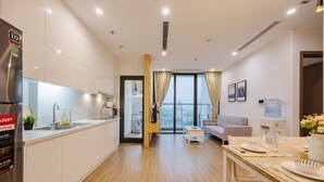 A modern apartment with a kitchen, dining area, and living room. It features a large window with curtains, a water dispenser, and a sofa. - Vinhomes Skylake Managed by Anstay Residence (Hanoi)