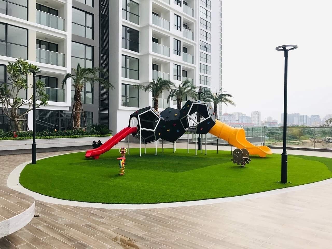 A playground with slides and climbing structures, surrounded by a green lawn and a building in the background.