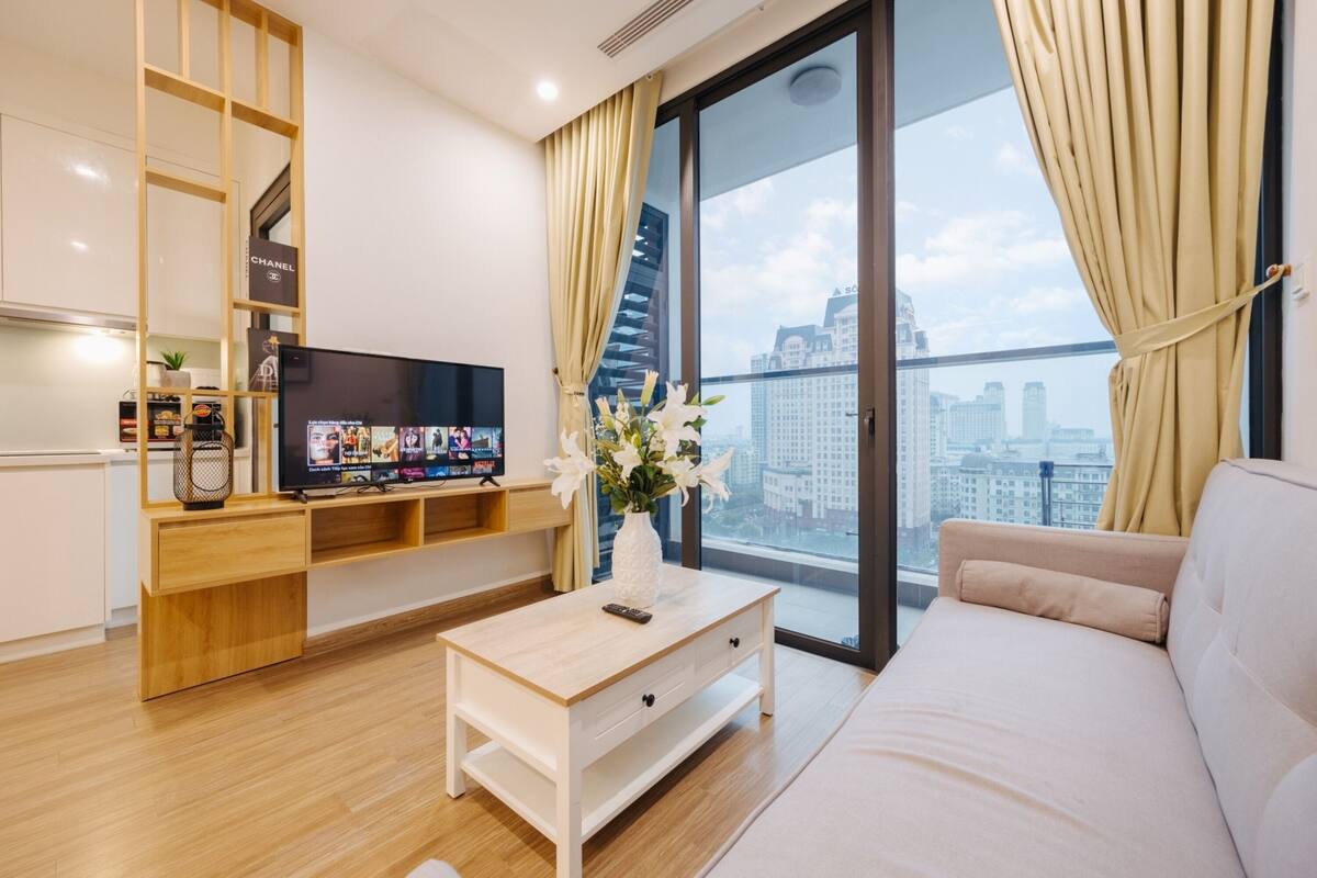 A modern living room with a flat-screen TV, a wooden coffee table, a sofa, and a large window with a city view.