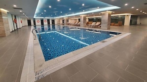 A modern indoor swimming pool with a geometric ceiling design, lounge chairs, and a tiled floor. - Vinhomes Skylake Managed by Anstay Residence (Hanoi)