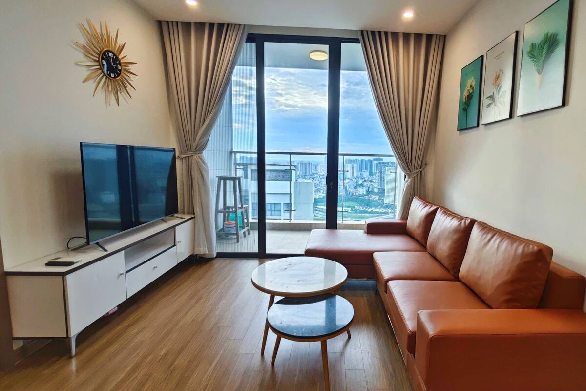 A modern living room with a large window, a flat-screen TV, a leather sofa, and a small round table.