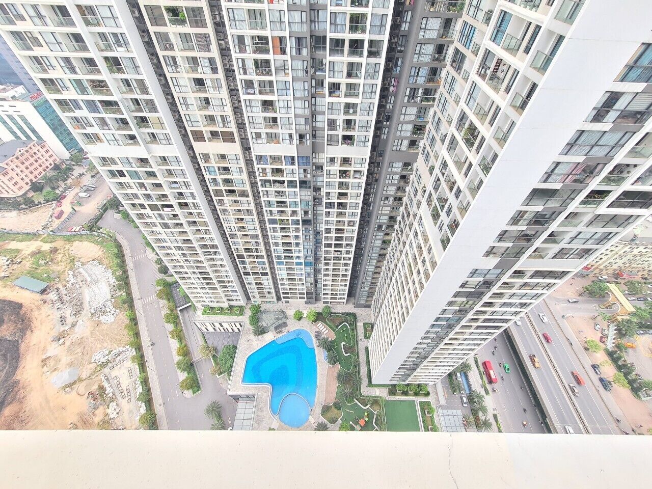 Un edificio residencial de gran altura con varios pisos, una piscina y una zona ajardinada con árboles.