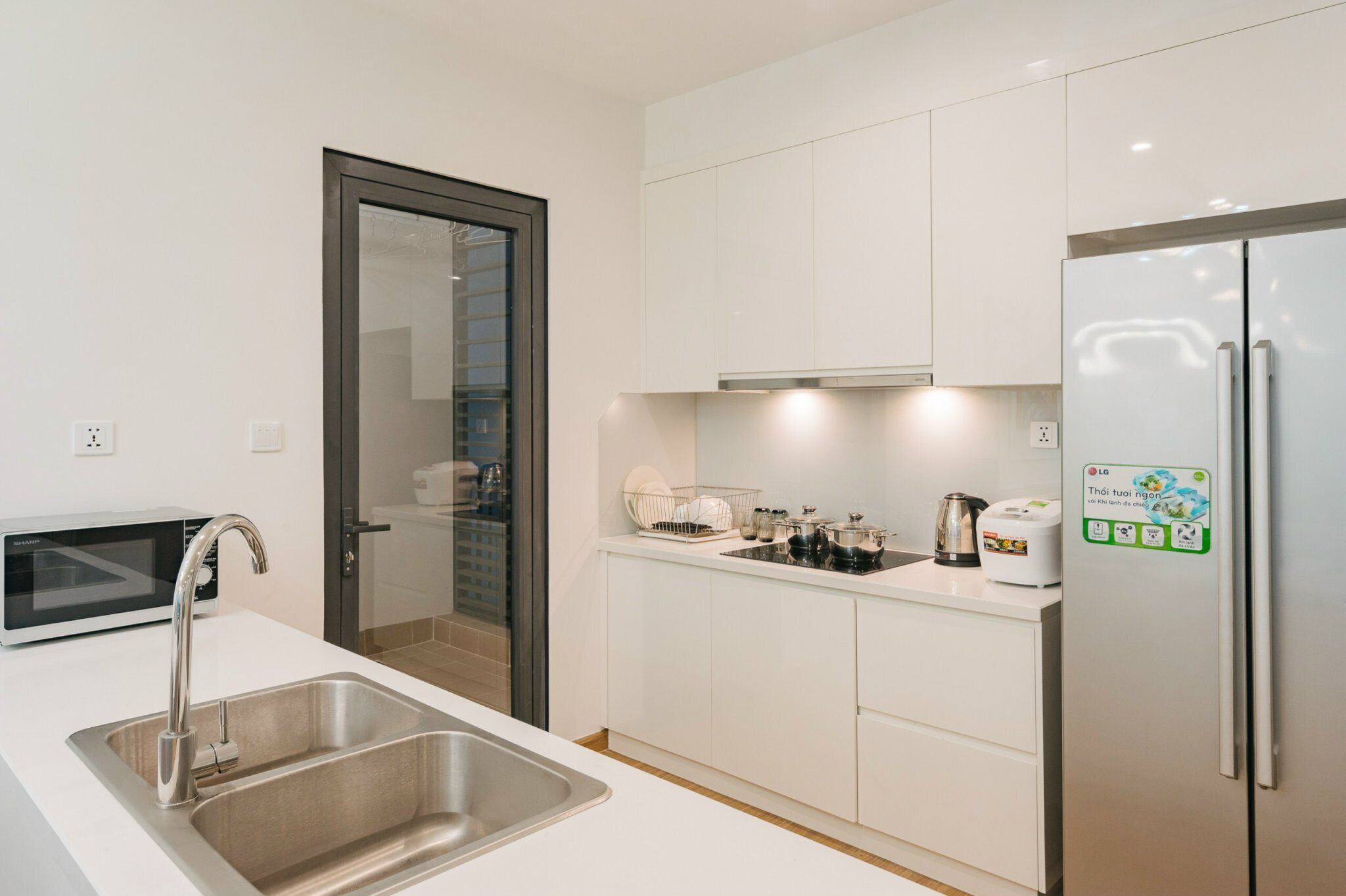 A modern kitchen with white cabinets, a stainless steel sink, a built-in microwave, a refrigerator, and a toaster.