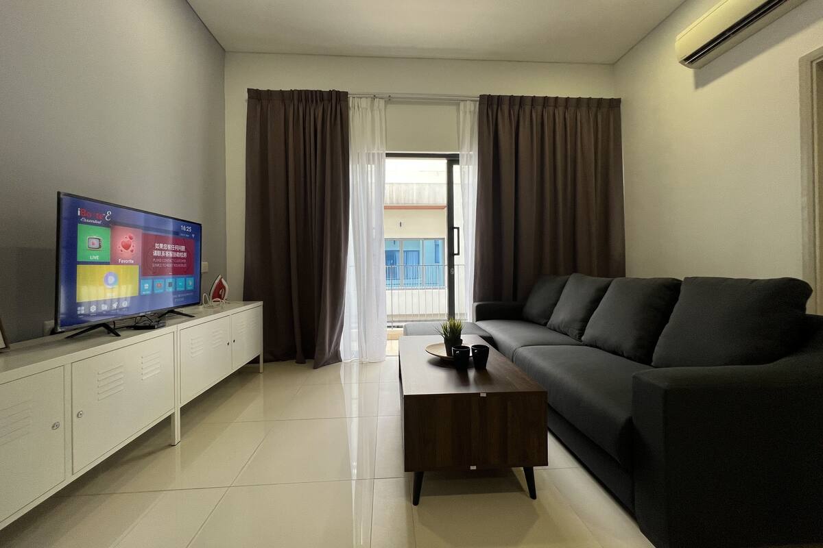 Ein modernes Wohnzimmer mit Fernseher, einer Couch, einem Couchtisch und einer Glastür, die auf einen Balkon führt.