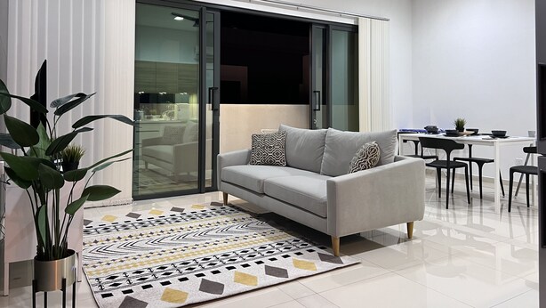 A modern living room with a grey sofa, a patterned rug, and a dining area with a table and chairs. - Desa Parkcity Plaza Arkaida Suite KL (Kuala Lumpur)