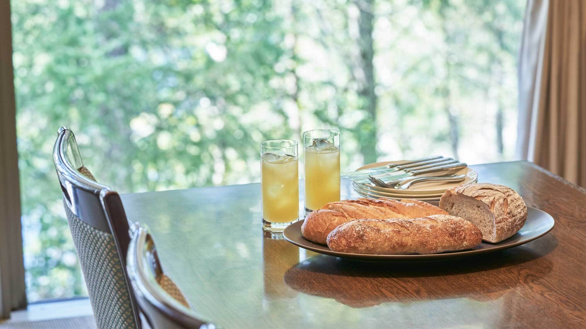 Una mesa con un plato de pan, dos vasos de té helado y una silla.