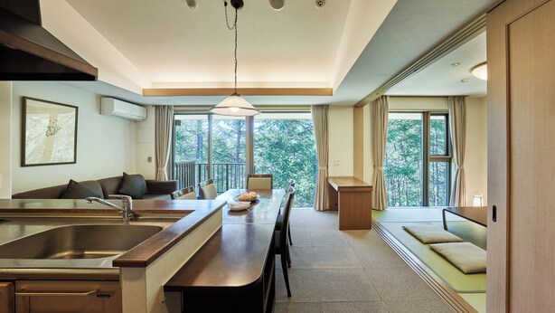 A modern kitchen with a built-in stove, a dining area with a low table and chairs, and a view of the outdoors through large windows. - Tokyu Vacations Tateshina (Chino)