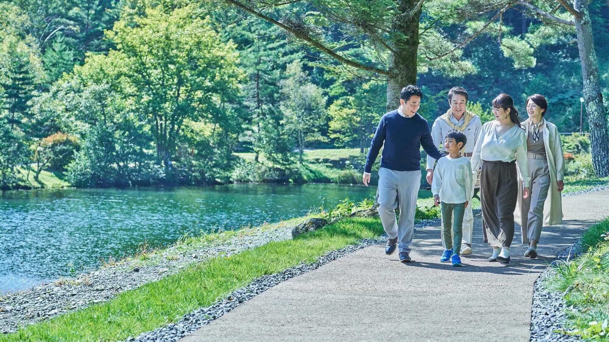 Una familia camina por un sendero pavimentado junto a un lago, rodeada de abundante vegetación.