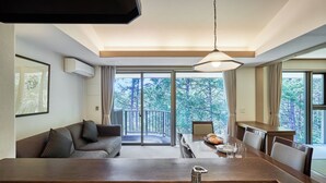 A modern hotel room with a large dining table, a sofa, and a view of the forest through large windows. - Tokyu Vacations Tateshina (Chino)