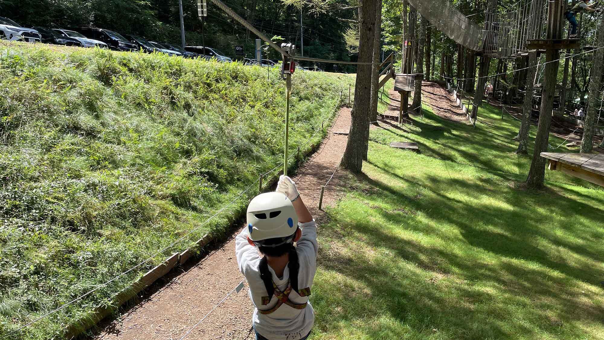 A person in a white helmet and safety gear on a rope bridge in a wooded area.