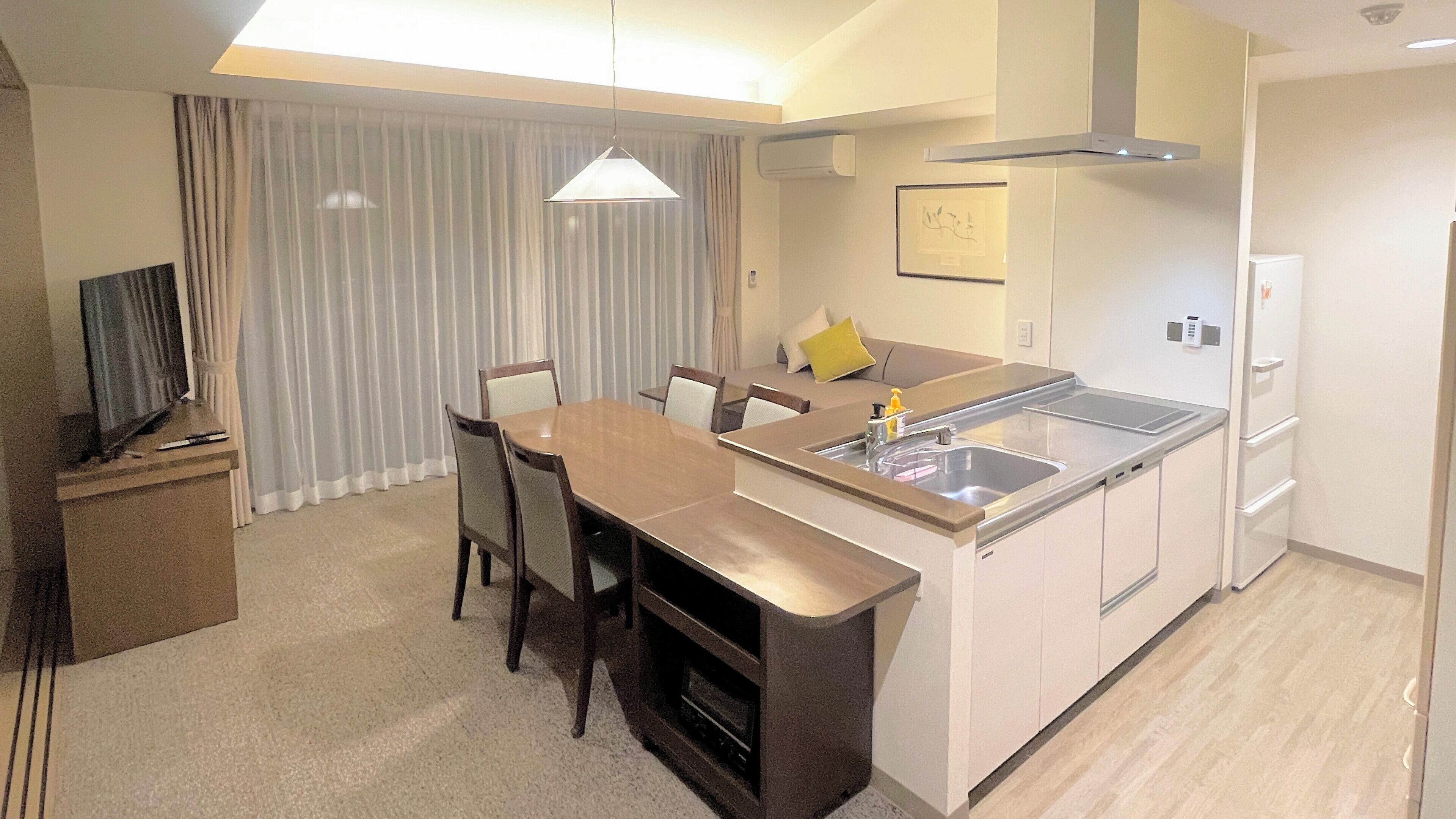 A compact hotel room with a kitchenette, a dining area, and a seating space.