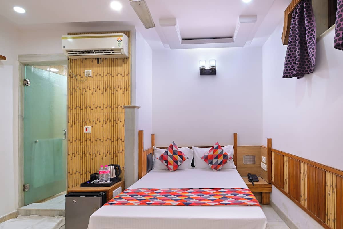 Une chambre d’hôtel comprenant un lit, une tête de lit en bois, une table de chevet, un bureau, un climatiseur, un luminaire fixé au mur et un mur recouvert de panneaux en bambou.