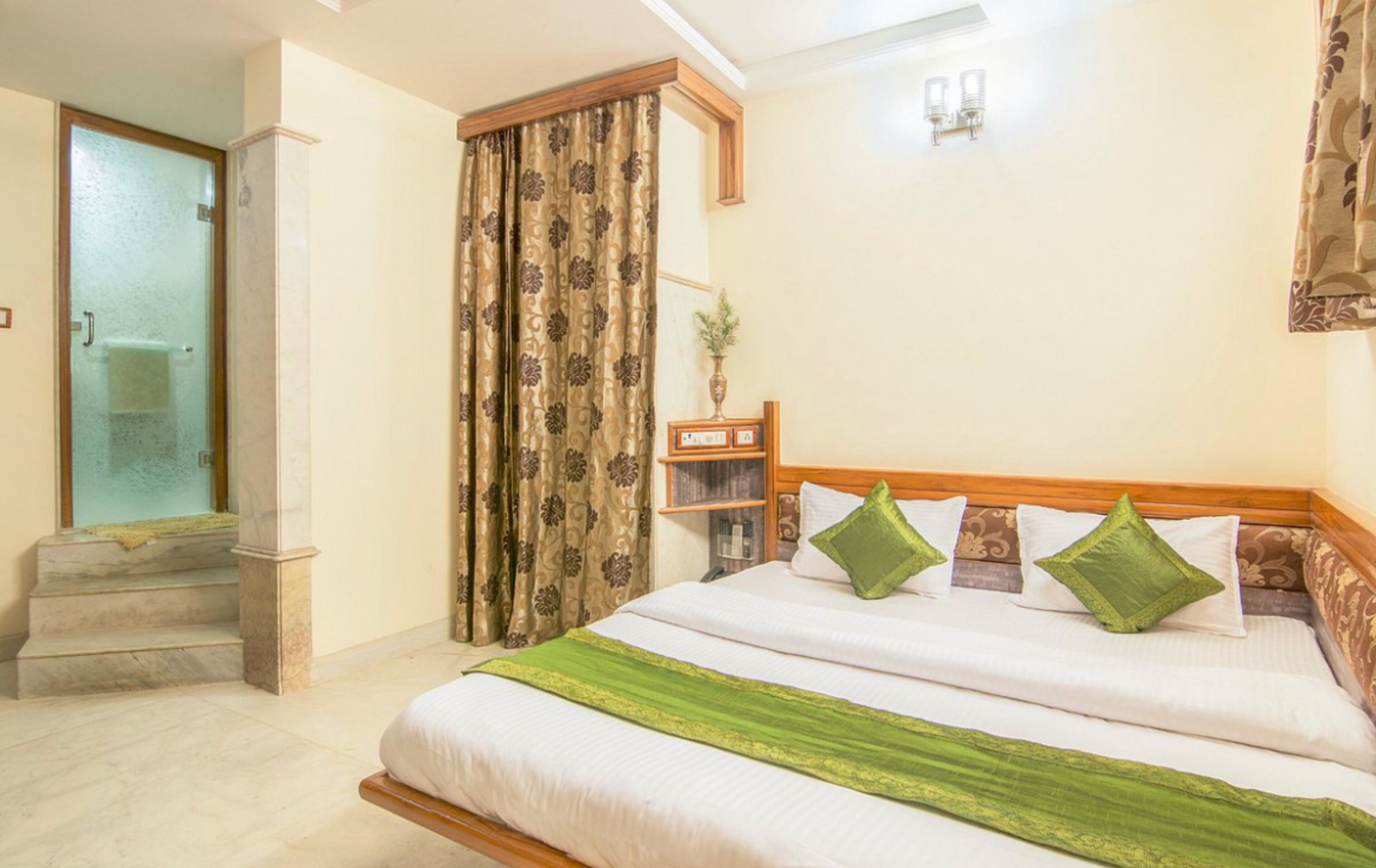 Una camera d'albergo con un letto, un comodino, uno specchio, una finestra con tende e un bagno con doccia e WC.
