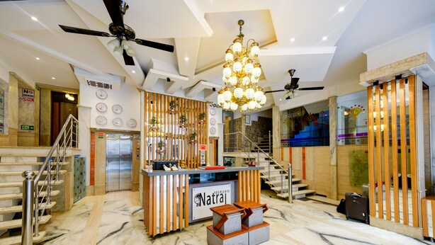 Een hotel lobby met marmeren vloeren, een receptiebalie, een trap en een plafondventilator.