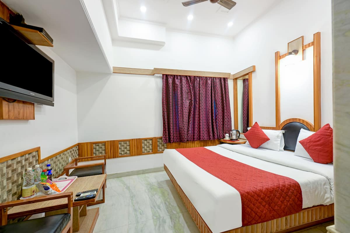 Une chambre d’hôtel avec un lit, une télévision, un bureau avec une chaise et une fenêtre avec des rideaux.