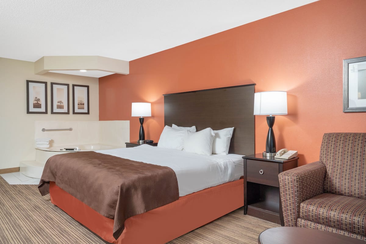 A hotel room with a large bed, two bedside lamps, a chair, and a small table.