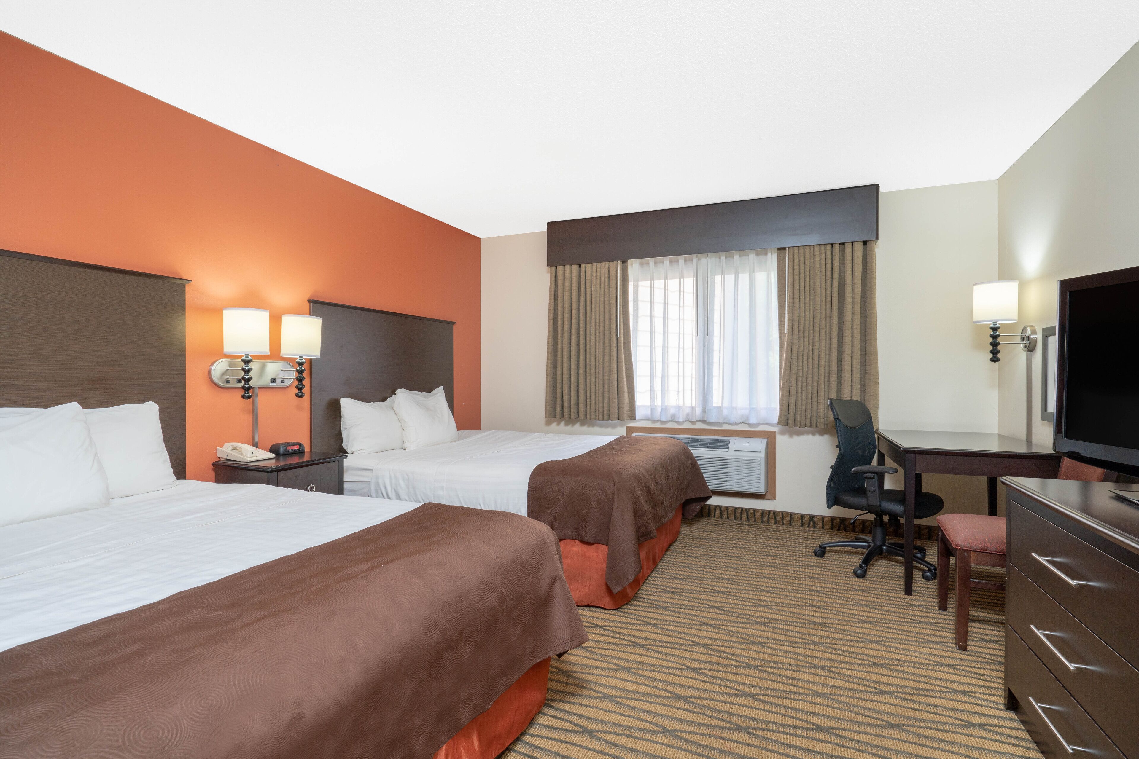A hotel room with two beds, a desk, a chair, a television, and a window with curtains.