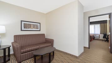 A hotel room with a brown patterned sofa, a small round table, a framed picture on the wall, and a carpeted floor.