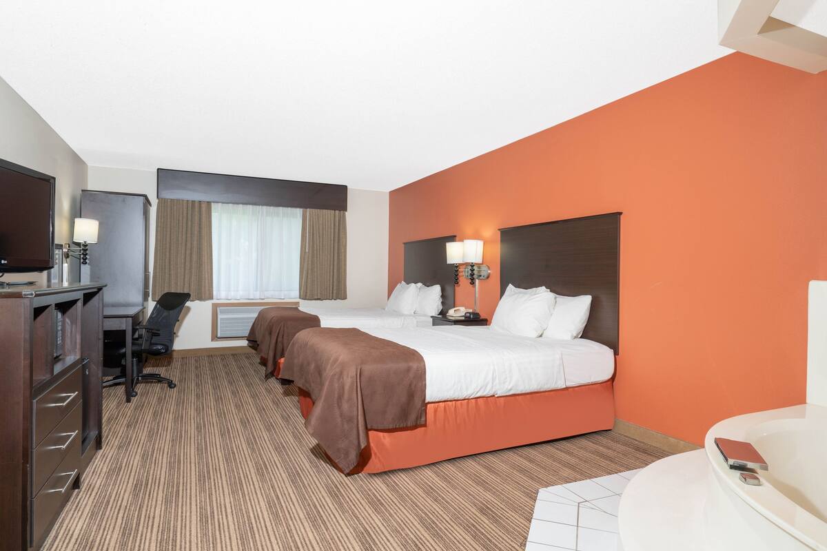 A hotel room with a large bed, two bedside tables with lamps, a desk with a chair, a TV, and a bathroom with a bathtub.