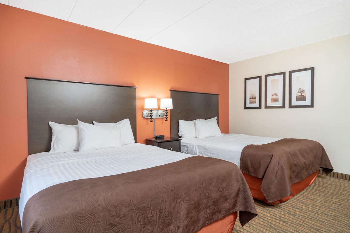 A hotel room with two beds, a nightstand with lamps, and framed pictures on the wall.