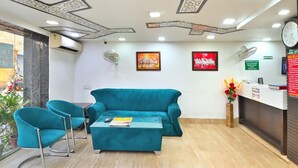 A reception area with a teal sofa, two matching armchairs, a coffee table, a reception desk, and a clock. - The Bella Vista – Traveler's Choice Awarded (New Delhi)