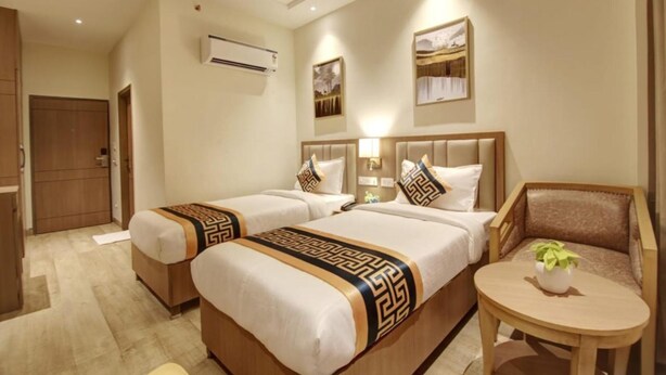 A hotel room with two beds, a small round table, a chair, and a wall-mounted air conditioner. - The Bella Vista – Traveler's Choice Awarded (New Delhi)