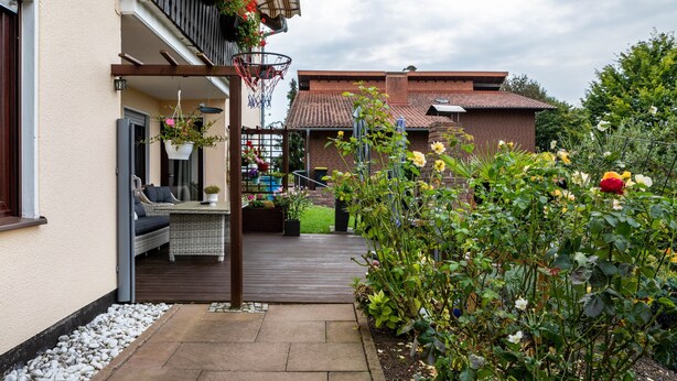 Propiedad residencial con balcón, mobiliario de exterior y jardín con flores.