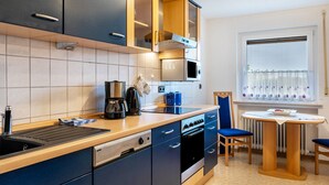 Cocina moderna con microondas, cafetera y horno. Hay un comedor con mesa y sillas.
