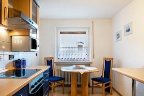 Une cuisine compacte équipée d’une cuisinière, d’un four à micro-ondes et d’un four traditionnel, d’une table à manger avec des chaises et d’une fenêtre avec des stores.