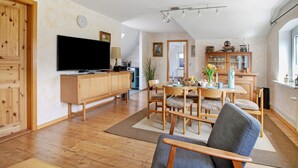 Een ruime woonkamer met een flatscreen televisie, houten meubels, een eettafel met stoelen en een keuken op de achtergrond.