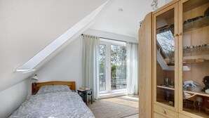 Een slaapkamer met een bed, een houten garderobe, een kleine tafel met een lamp en een glazen schuifdeur naar buiten.