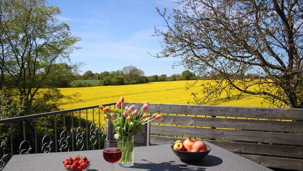 Een tafel met een fruitschaal, een glas rode wijn en een bloevas.