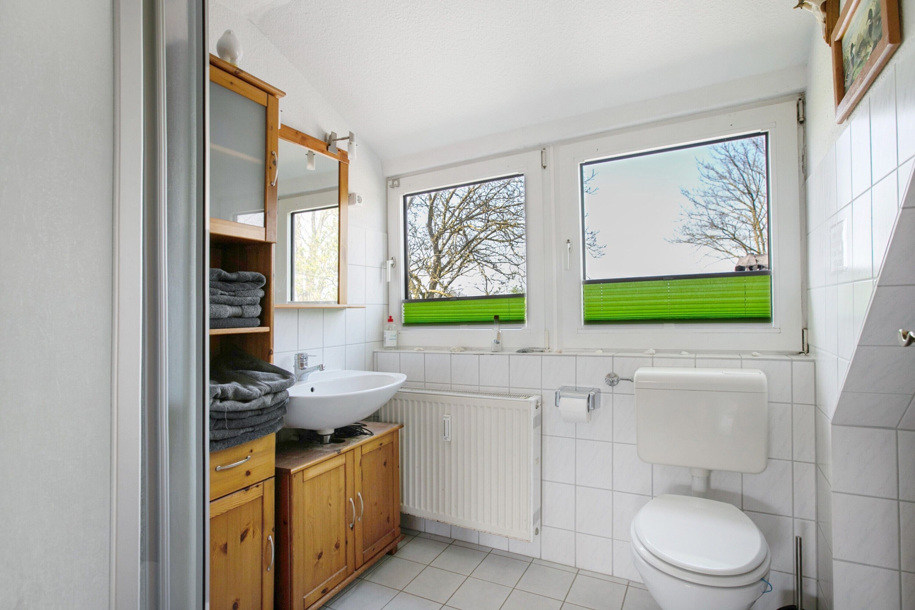 Une salle de bain avec un lavabo blanc, un meuble en bois, des toilettes et une fenêtre donnant sur des arbres.
