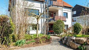 Een modern, twee verdiepingen hoog gebouw met een grindpad, een kleine tuin met diverse planten en een stenen muur.