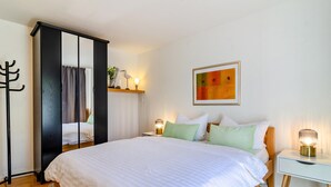 Een slaapkamer met een bed, nachtkastjes, een kapstok, een wandplank en een lijst met een afbeelding.