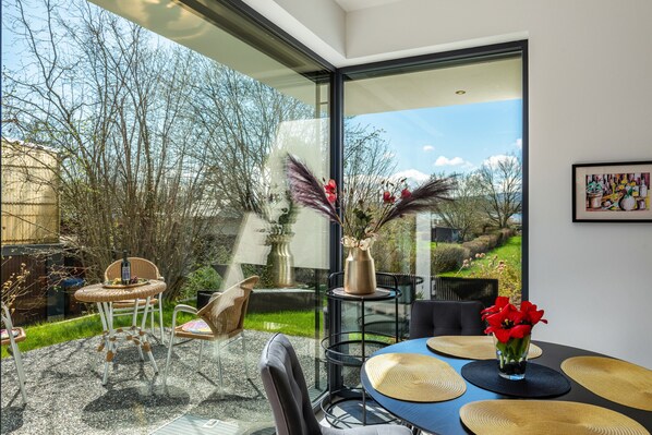 A modern dining area with a glass table, wicker chairs, and a vase of red flowers.