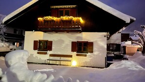 Un chalet enneigé doté d’un balcon, de volets en bois et d’un éclairage extérieur.