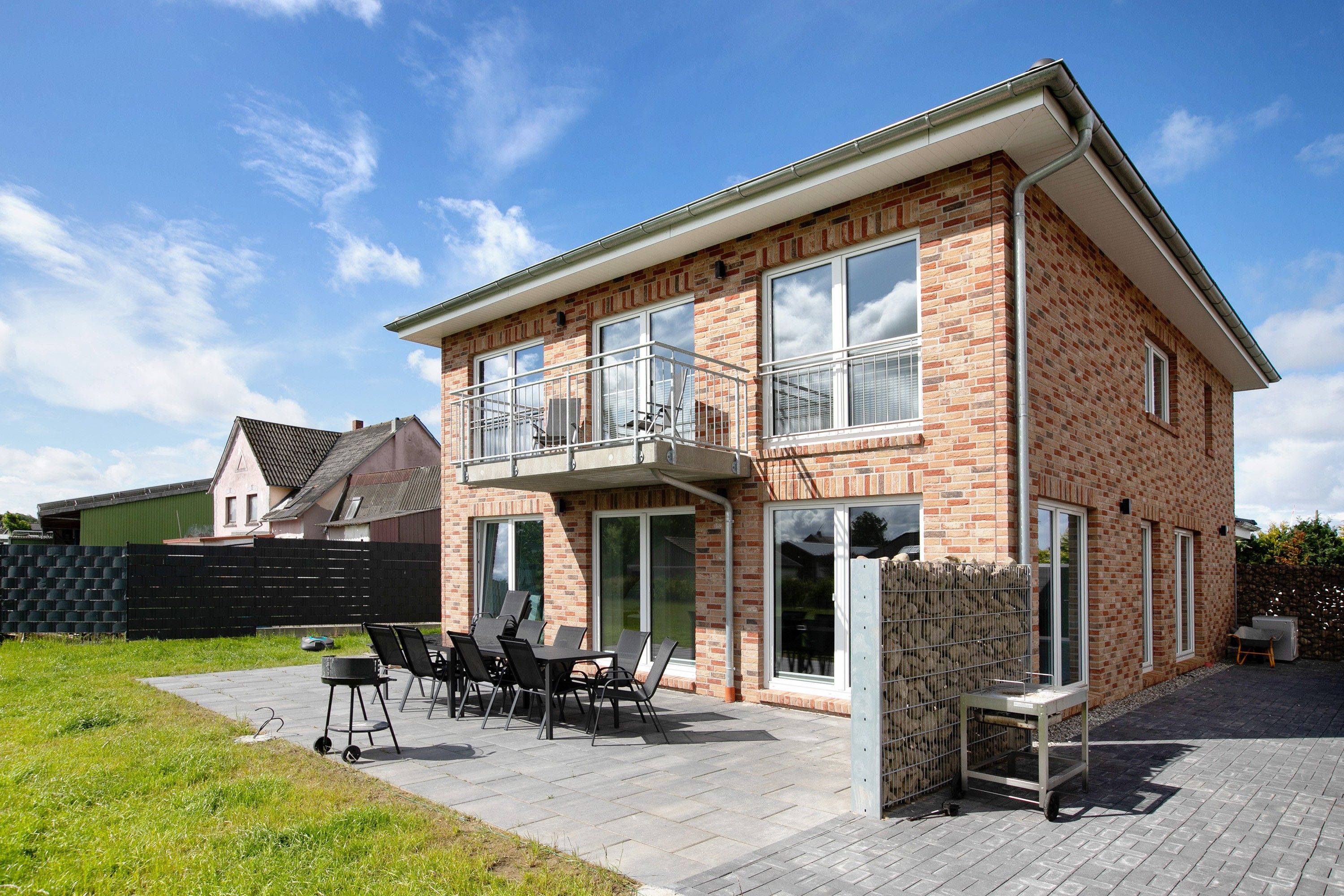 A two-story house with a balcony, a patio with outdoor furniture, and a brick exterior.