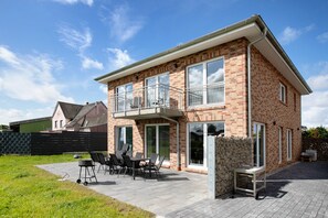 Ein zweistöckiges Haus mit Balkon, einer Terrasse und Gartenmöbeln sowie einer Ziegel-Fassade.