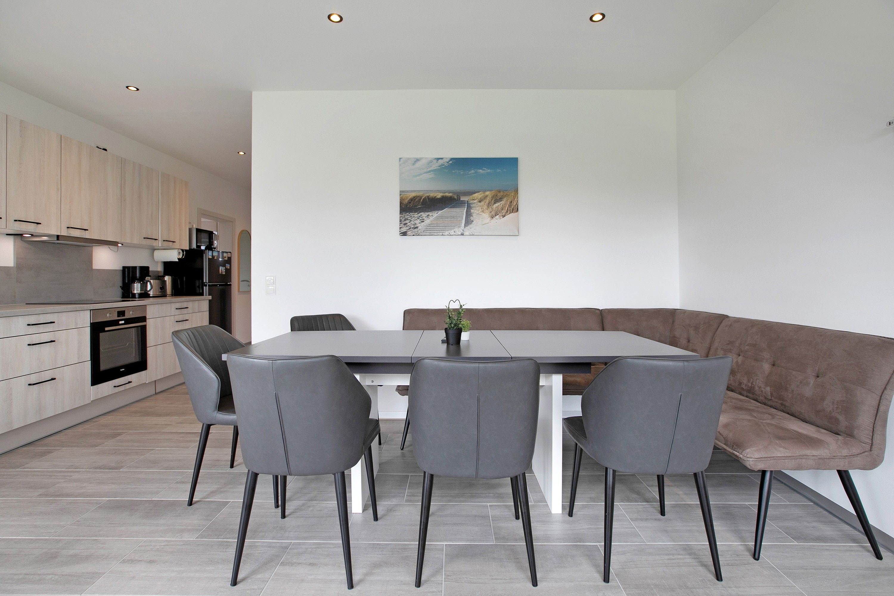 Una cucina moderna con elettrodomestici integrati, un'area pranzo con una panca e sedie, e un quadro appeso al muro.