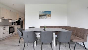 Una cucina moderna con elettrodomestici integrati, un'area pranzo con una panca e sedie, e un quadro appeso al muro.