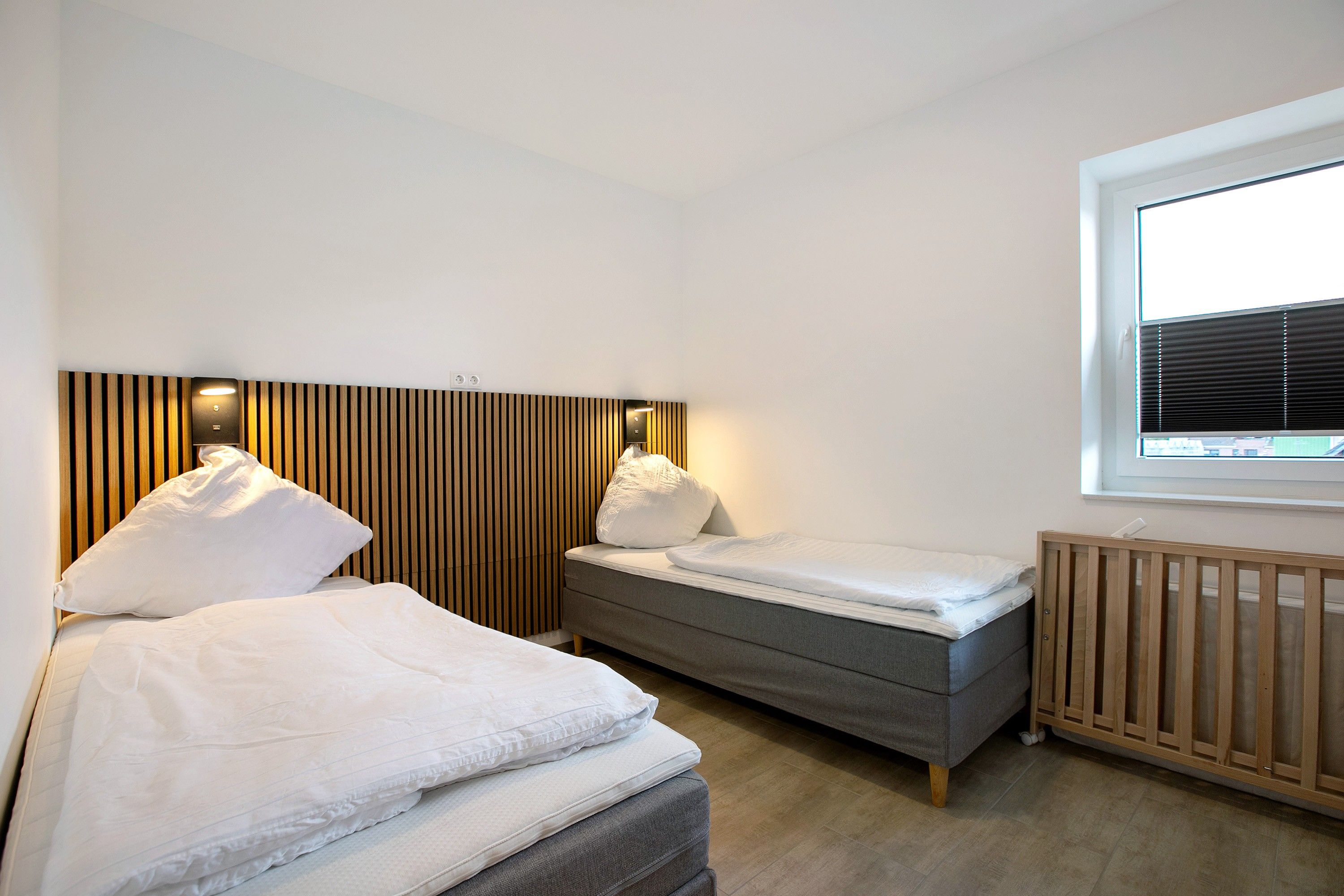 Un dormitorio con una cama grande, una cama más pequeña, una ventana con persianas y un cabecero de madera.